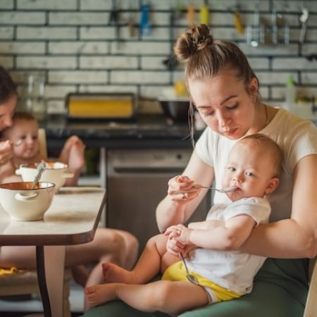 two-young-mothers-together-feed-their-happy-babies-milk-porridge-kitchen_114354-1228